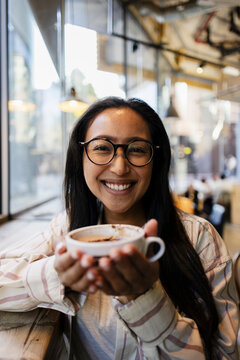 Smiling woman with glasses enjoying coffee in a cafe indoors