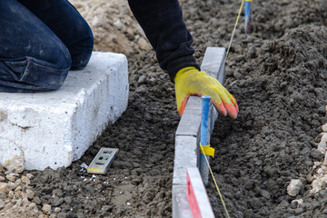 Close-up of construction worker leveling concrete and placing edging pin kerb on construction site