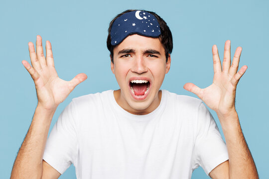Close up calm young scared man wear pyjamas jam sleep eye mask rest relax at home spread hands look camera scream isolated on plain pastel blue cyan background Woke up from terrified freddy nightmare