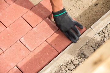 Close-up of builder laying red paving bricks on newly constructed pathway