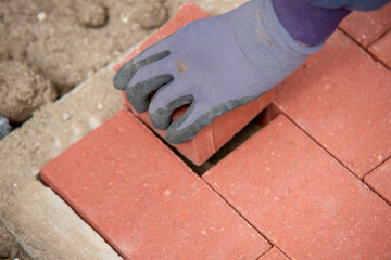 Close-up of builder fitting red paving bricks into  pattern on sandy base