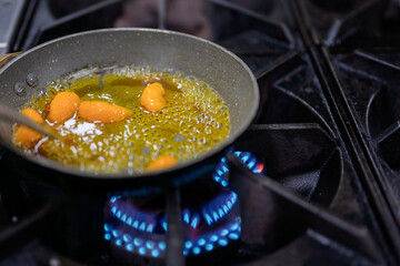 Close-up of orange segments simmering in caramel syrup on gas stove, golden color with boiling bubbles in shallow depth of field.