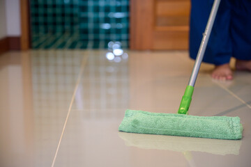 Close-up shot of a green microfiber mop cleaning shiny tiled floor indoors, captured in soft natural light with shallow depth of field and reflection on surface.