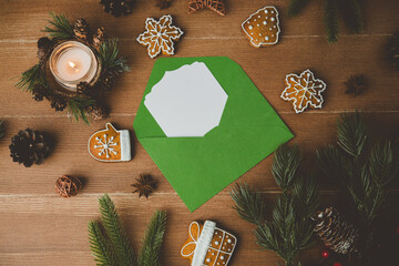 Christmas cookies and lit candle on wood table with green envelope and pine branches