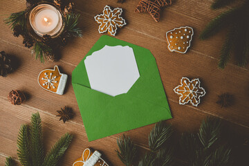 Green envelope with blank card and holiday cookies on wooden surface with candle