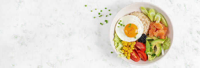 Poke bowl featuring fresh ingredients like salmon, corn, avocado. tomatoes and a sunny side up egg on a light background. Top view