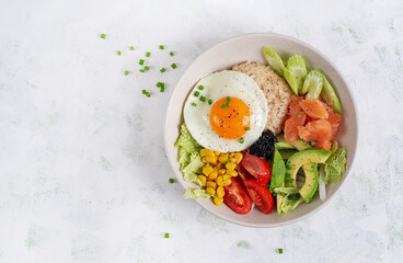 Poke bowl featuring fresh ingredients like salmon, corn, avocado. tomatoes and a sunny side up egg on a light background. Top view