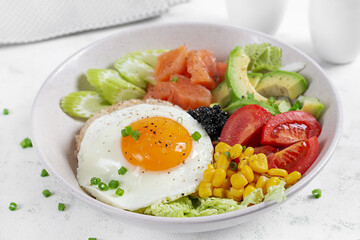 Poke bowl featuring fresh ingredients like salmon, corn, avocado. tomatoes and a sunny side up egg on a light background.