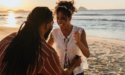 Joyful couple celebrating engagement on a beach at golden hour
