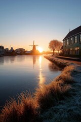 Obraz premium Serene sunrise over dutch village canal with windmill and frosty landscape