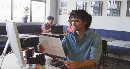 Reviewing man in teal shirt examining photographic print at coworking studio, with DSLR camera