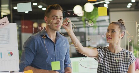 Teen girl drawing triangle with coworker watching on glass board in office, with sticky notes