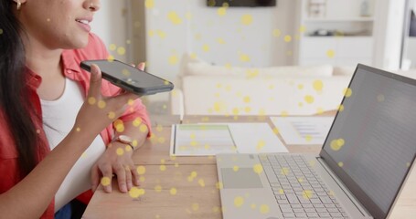 Red shirted woman dictating into smartphone at desk living room, with laptop, documents, copy space