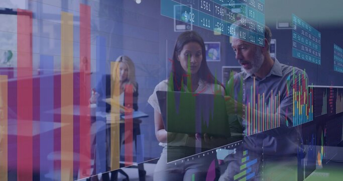 Discussing two professionals reviewing laptop data in open-plan office, with chart overlays