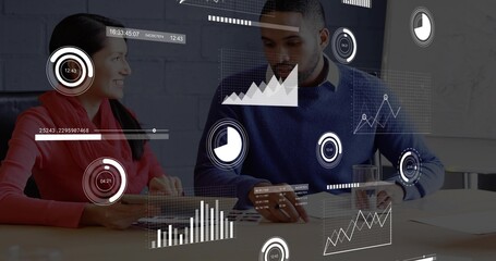 Sitting colleagues in business attire reviewing charts with data overlays at office table