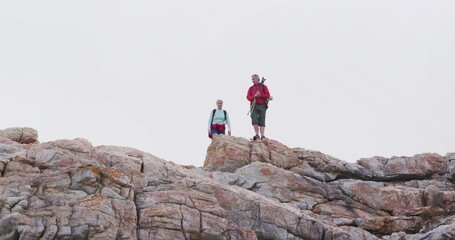 Standing hikers wearing red jacket and blue top scanning rocky ridge with backpacks and tripod