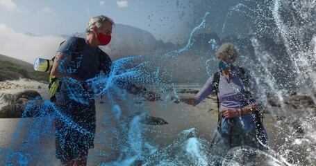 Standing senior hikers wearing masks on rocky seaside with hiking poles and digital water overlay