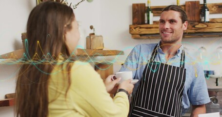 Serving barista wearing striped apron handing white coffee cup at shop counter, with coffee machine