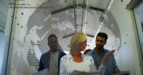 Discussing colleagues holding documents behind map partition in meeting area, with exposed ducts