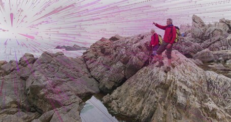 Pointing hiker and watching companion in red jackets on coast with backpacks and boots, copy space