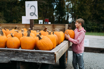 Preteen child choosing pumpkin from farm wagon