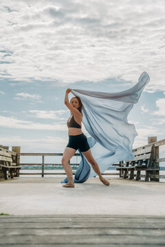 Dancer performing with flowing fabric on pier