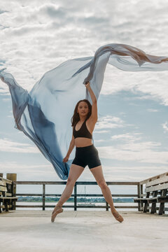 Dancer performing ballet en pointe on pier with fabric