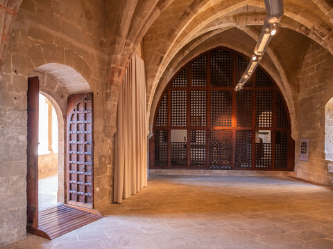 Castell de Bellver, Mallorca, spacious, arched stone hall features a wooden door with intricate lattice work, leading to a large window with similar design elements, Majorca