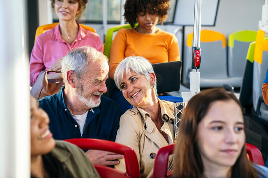 Diverse people traveling on a city bus. Focus on a happy senior couple interacting while other passengers use technology