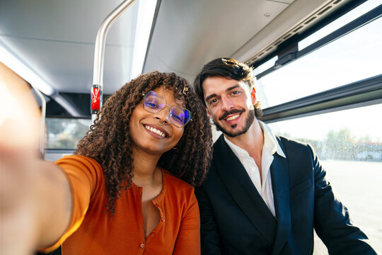 Happy diverse couple smiling, taking a selfie on a city bus, enjoying their urban commute and travel together