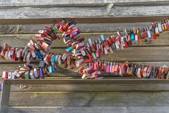 Love locks on wood. Colorful love locks attached to a wooden structure form a heart shape. Symbols of love and memories by the seaside. - Powered by Adobe