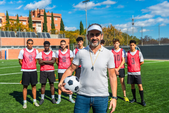 Male coach holding football with diverse soccer team