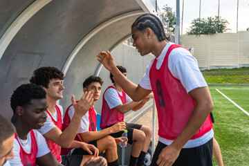Diverse soccer team high fiving in dugout, celebrating success