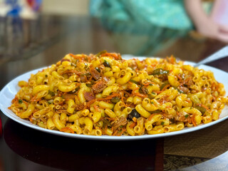 Closeup of a large platter of Desi-style chicken macaroni. A creamy, spicy pasta dish with shredded chicken and vegetables, popular as a quick, flavorful comfort meal.