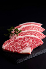 Close-up of premium Wagyu beef slices showcasing intricate marbling patterns. The raw meat is arranged neatly on a black slate surface with a garnish of fresh herbs, highlighting the luxurious texture