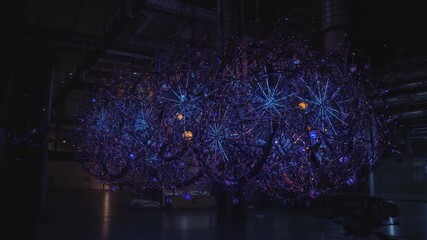 Kinetic LED sculpture pulsing-rotating bicycle wheel frames in factory hall, with blue-orange glow - Powered by Adobe