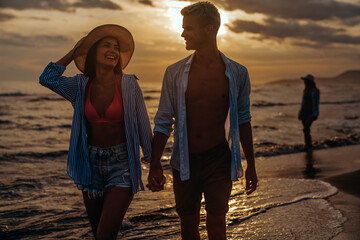 Young beautiful couple walks along the seashore at sunset. Honeymoon. Romantic trip.
