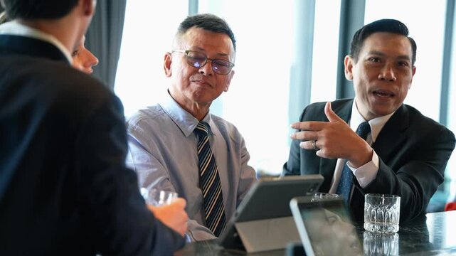 Asian businessmen collaborating in an informal corporate meeting, discussing successful business strategy and reviewing financial data on a digital tablet at hotel lounge - Powered by Adobe