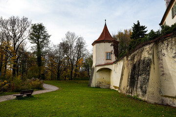 Blutenburg Castle in Munich with historical castle turret and defensive wall rising from lush green lawn, surrounding an autumn park with a winding path and bench © Sandra Alkado