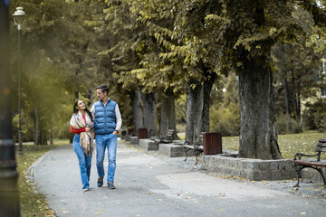 Obraz premium A couple enjoys a romantic walk through a picturesque autumn park, showcasing vibrant foliage and a serene atmosphere, perfect for capturing love and companionship in nature.