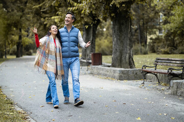 The couple is engaged in a lively discussion while walking hand in hand, radiating positivity and joy, surrounded by the vibrant colors of nature in an autumn setting.