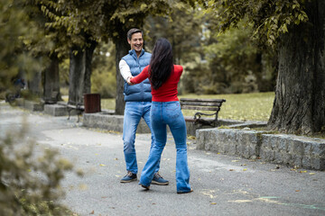 A happy couple dances together in a picturesque park, holding hands and enjoying the beauty of the outdoors, symbolizing love, joy, and connection in their relationship.