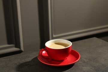 Red cup of aromatic coffee and saucer on dark textured table