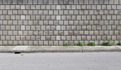 Grunge concrete square tile wall at roadside. Worn sidewalk and street in front. Background for copy space.