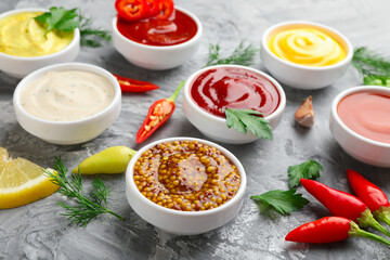 Different sauces in bowls and ingredients on grey textured table, closeup