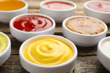 Different sauces in bowls on wooden table, closeup