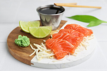 Fresh salmon sashimi with sliced radish, wasabi, lime and soy sauce on light table, closeup