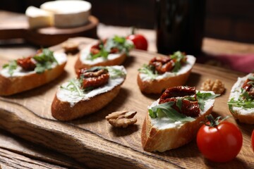 Delicious bruschettas with cream cheese, sun-dried tomatoes and arugula served on wooden table, closeup
