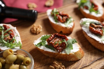Delicious bruschettas with cream cheese, sun-dried tomatoes, arugula and bottle of wine on wooden...
