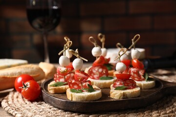 Delicious bruschettas with salami, mozzarella and tomatoes served with red wine on table, closeup